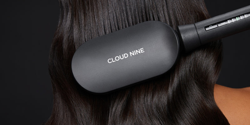 Close up of the Hot Brush straightening wavy dark hair. The CLOUD NINE logo is seen on the back of the product.